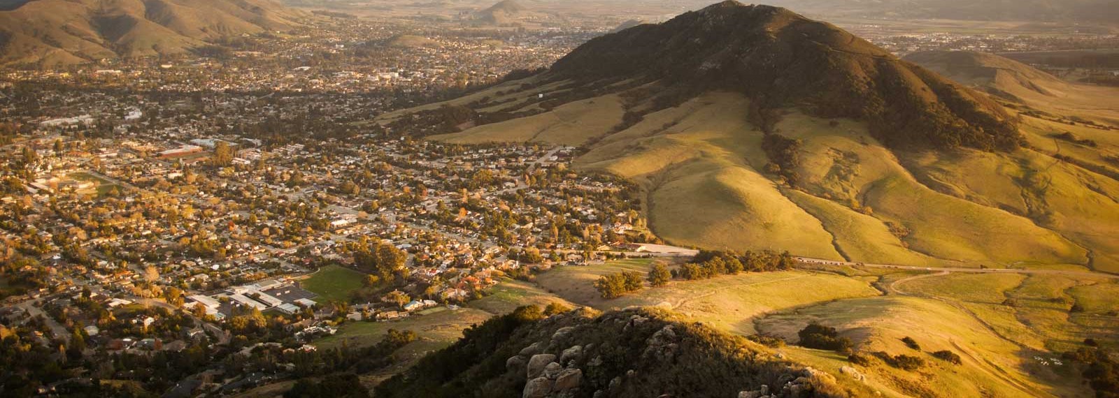 Aerial view of a coastal town nestled in green and golden hills at golden hour
